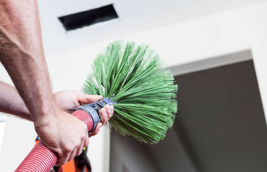 A man attaching a green brush to the end of a hose.