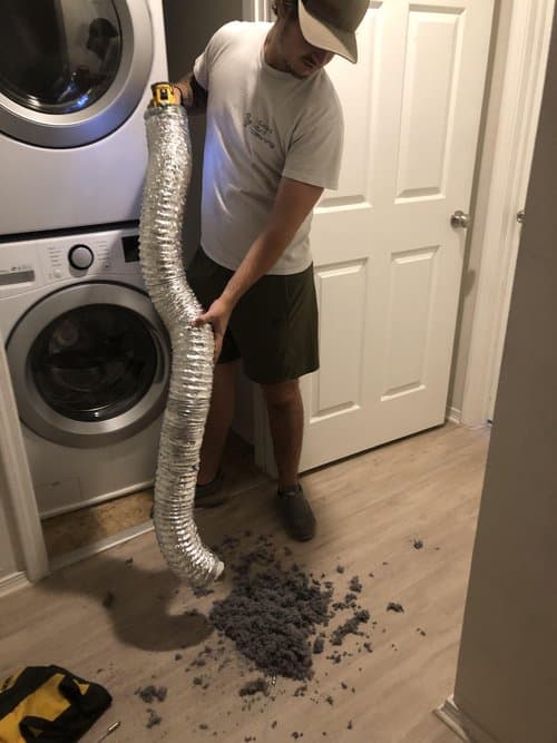 A man performing dry vent cleaning in a laundry room.