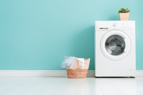 Interior of laundry room with a washing machine on bright teal wall background.